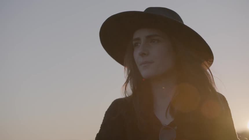 Woman wearing a hat next to a road at sunset
