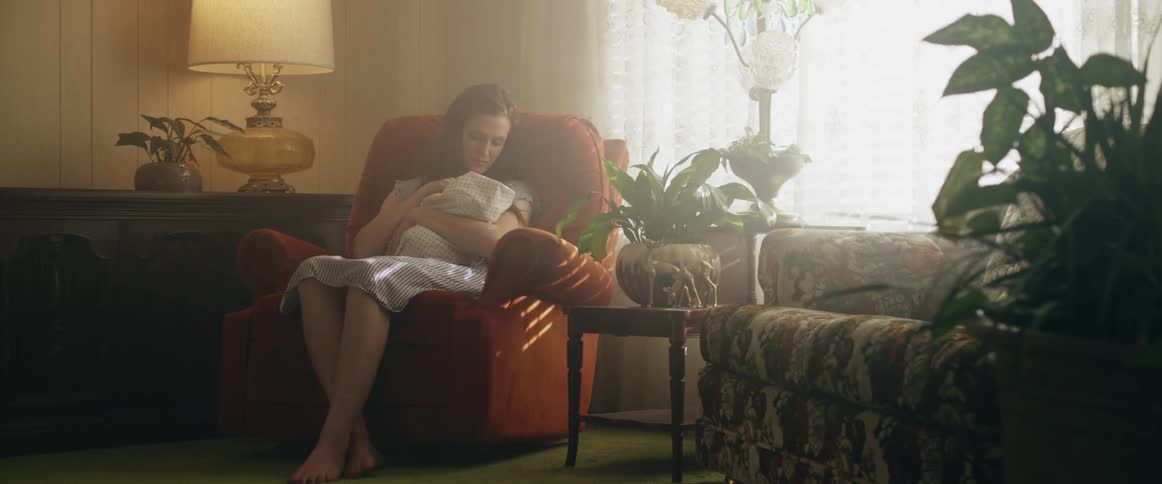 Mother sits in chair in living room holding baby in her arms