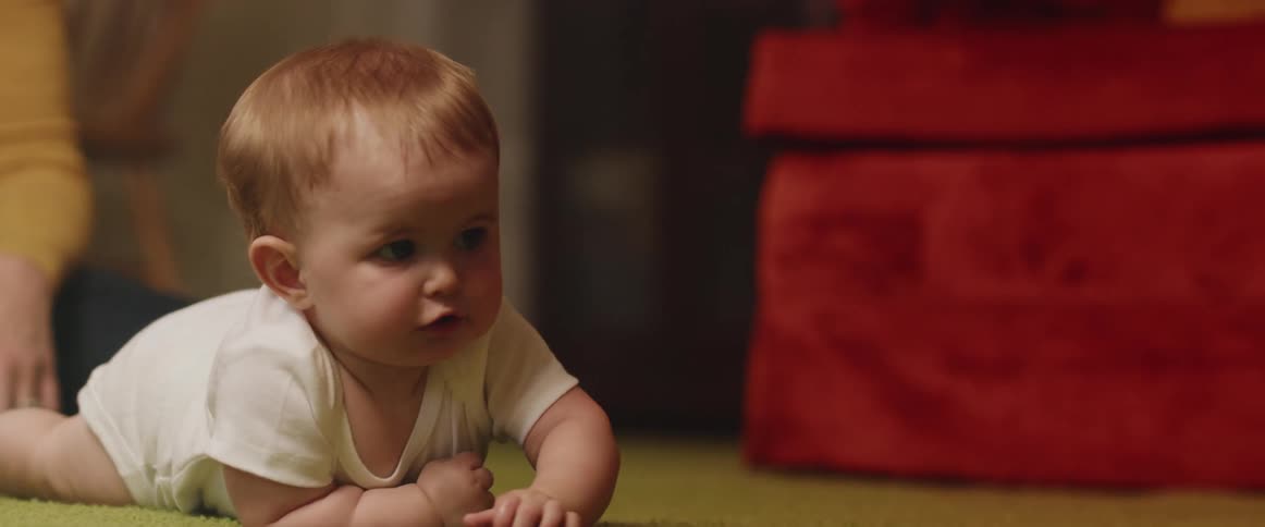 Parent watches baby try to crawl across living room carpet