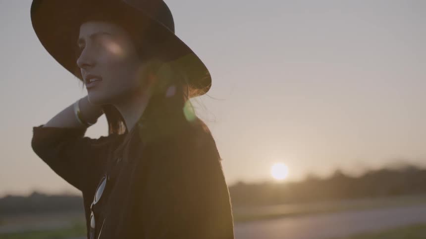 Woman wearing a hat next to a road at sunset