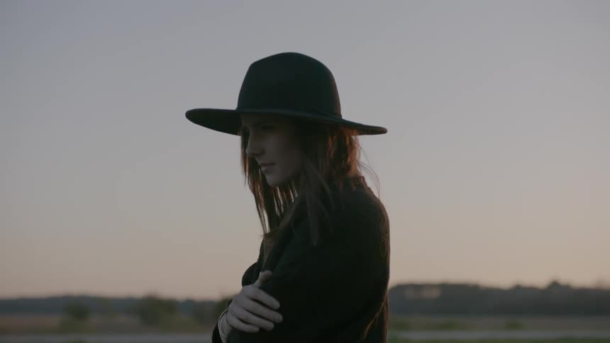 Woman wearing a hat next to a road at sunset