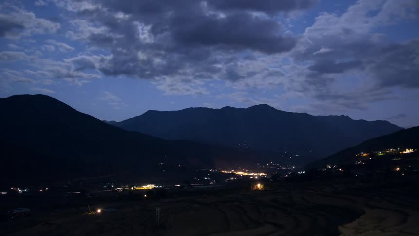 Time lapse of clouds floating over mountains and city lights