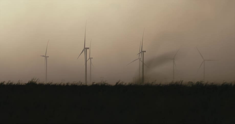 Wind turbines spin in a grassy field on a windy day under a cloudy sky