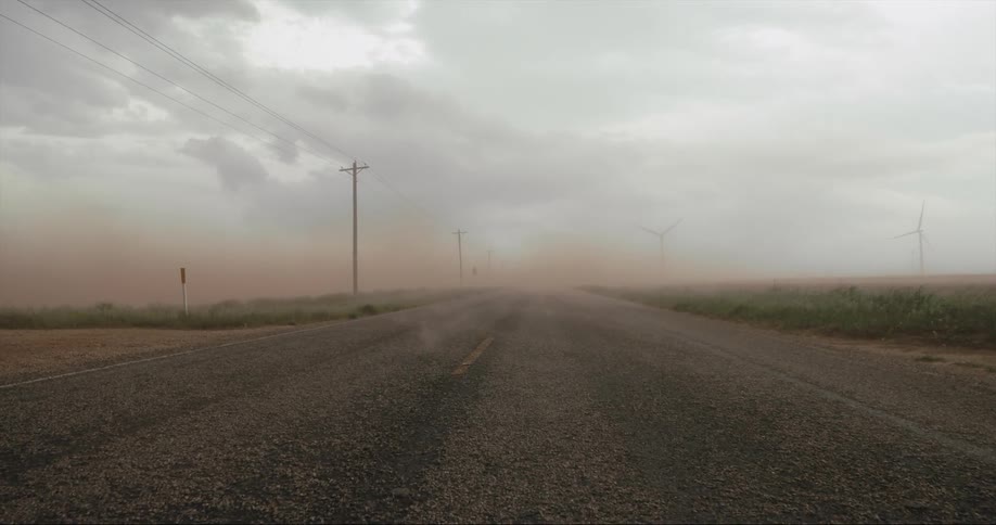 Fog rolling across a road next to a windfarm on a grassy field