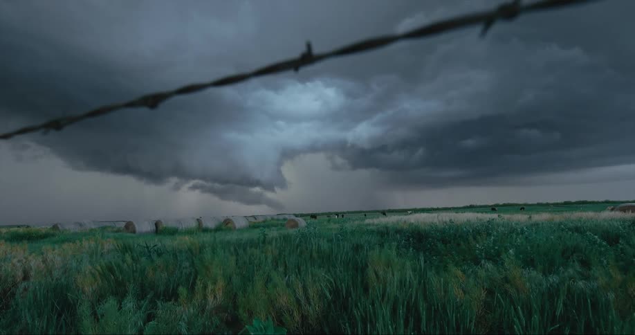 Massive storm clouds hover in the sky above a wide open grassy plain