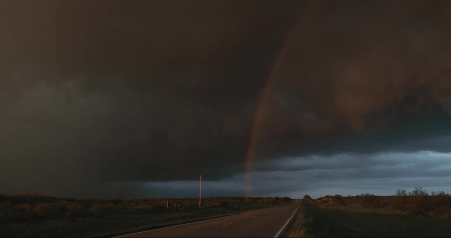 A rainbow dark storm clouds and a flash of lightning over a grassland