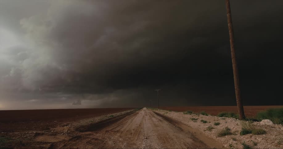 Dirt road leads between field to dark storm clouds on the horizon