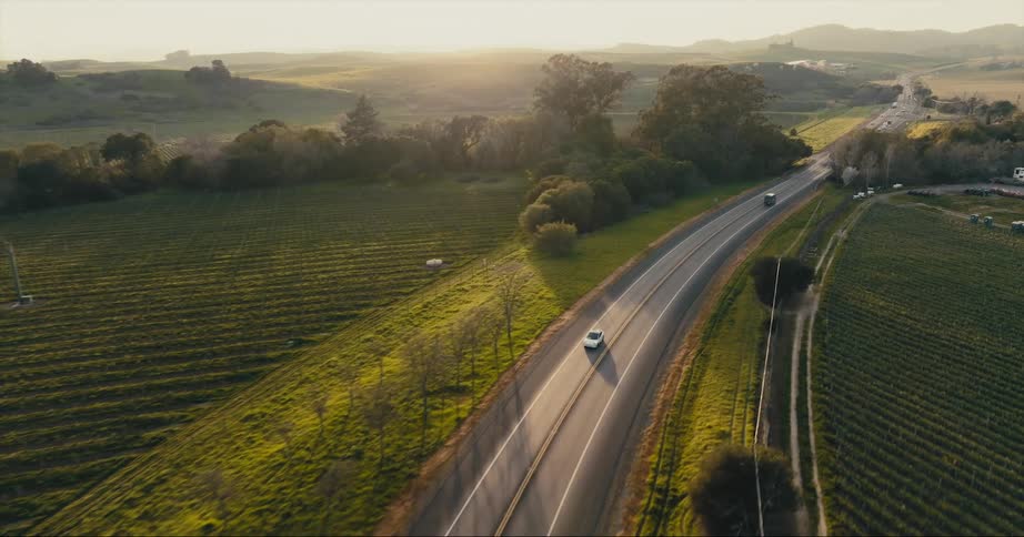 A vehicle travels along a road through a vast countryside during the day