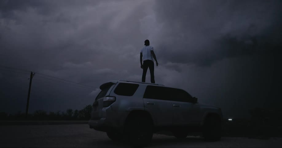 A man stands on the top of his sport utility vehicle during a storm