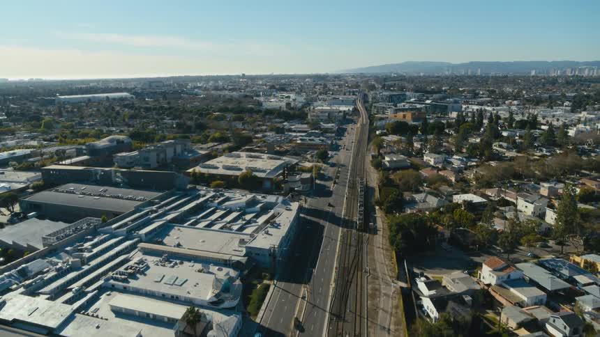 A train travels on tracks next to neighborhood streets past stores and homes