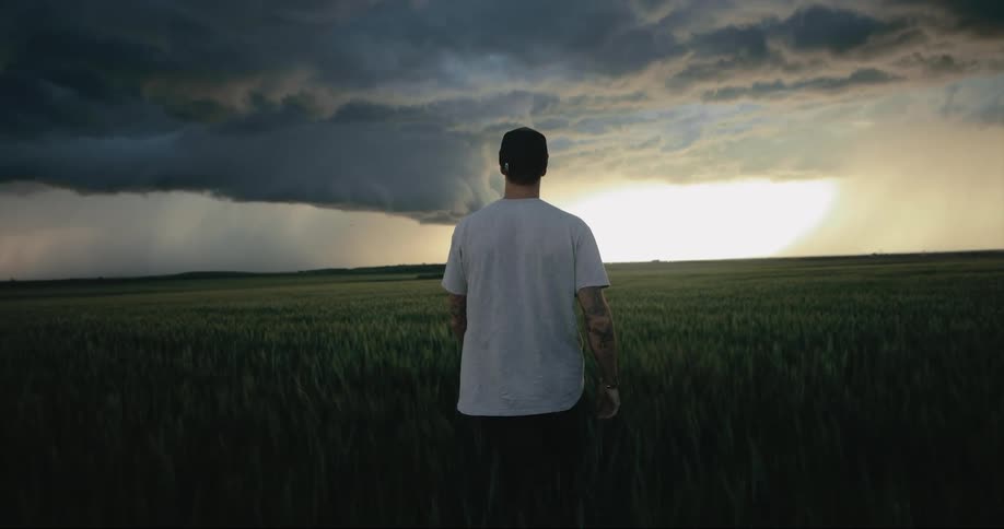 A man walks across a grassland when dark storm clouds are in the sky