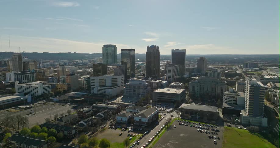 Cars parked on the city streets near the buildings and skyscrapers under a sunny blue sky