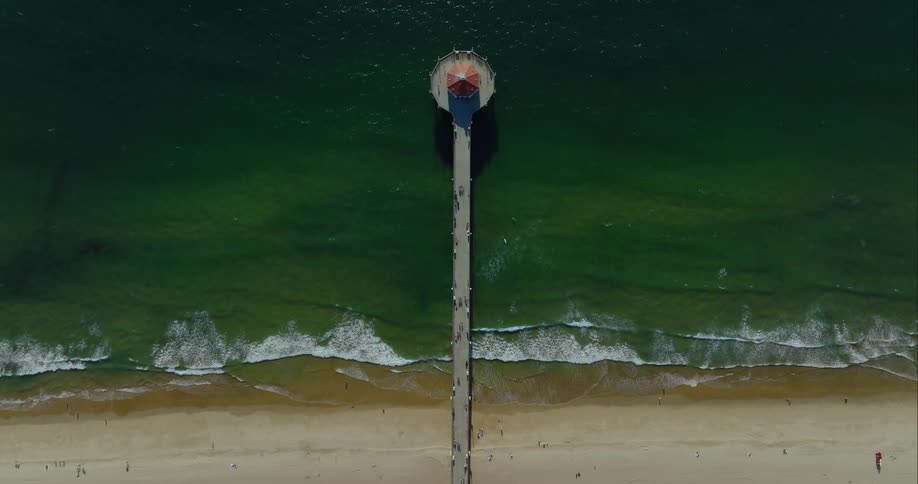 People walk on a pier with a gazebo as waves come to a sandy shore