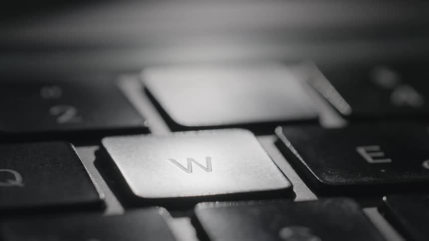 A finger presses the w key on a laptop keyboard