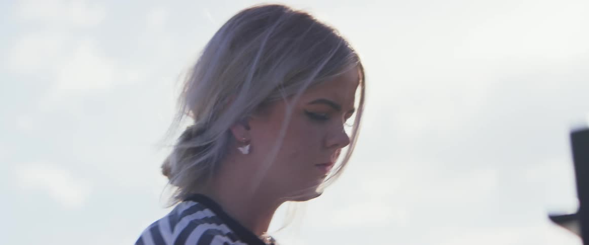 A young woman with blonde hair and a striped shirt walks outdoors on a sunny day