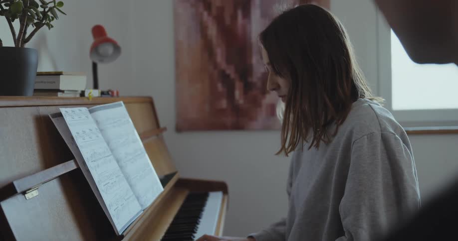 Woman with brown hair and gray shirt plays piano with man in room