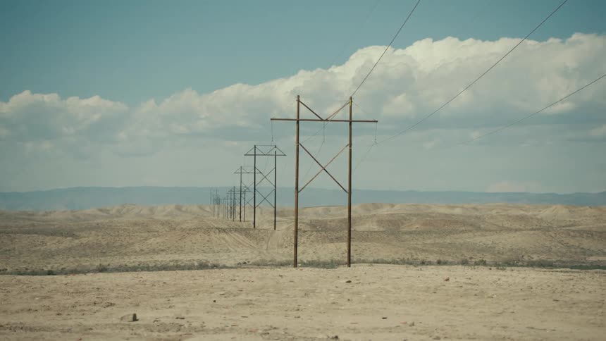 Power towers and lines in a desert landscape under a blue sky with white clouds