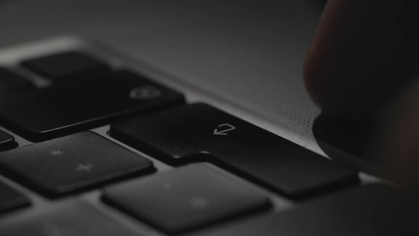 A person uses a finger to press the return key on a computer keyboard