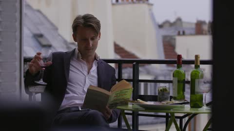 Man holding a glass of wine while reading on an outdoor dining terrace