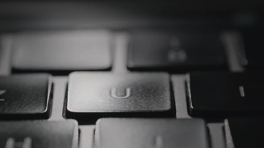 A finger presses the u key on a laptop keyboard