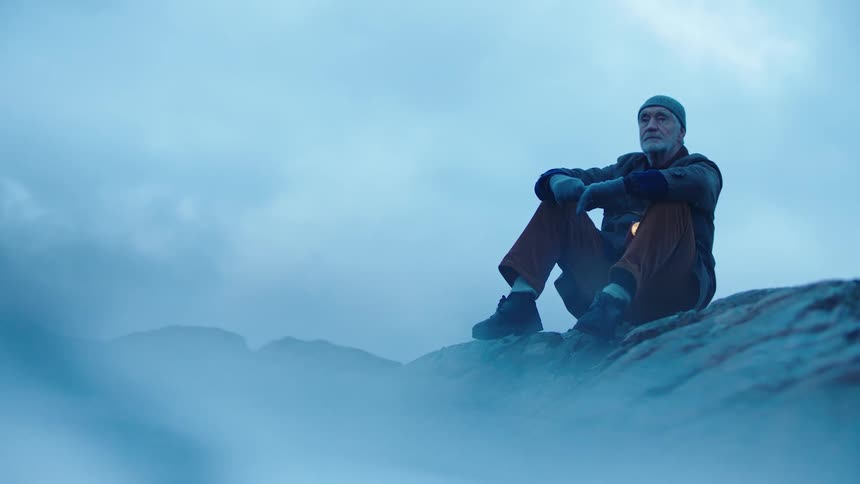 Elderly man wearing a toque and gloves sits on top of a snowy mountain