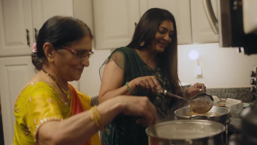 Mother and adult daughter smile as they cook in kitchen together