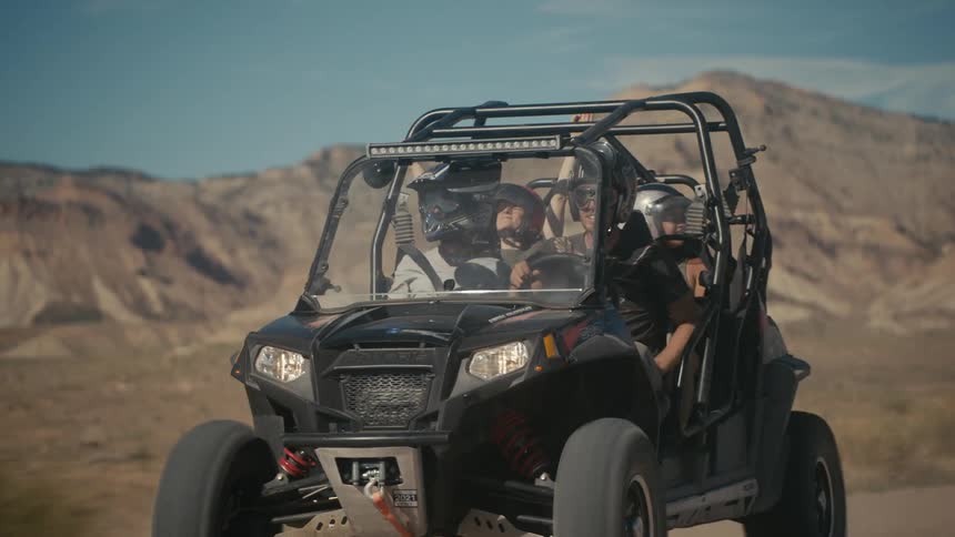 A passenger in a dune buggy raises her arms in excitement as the atv travels in the desert
