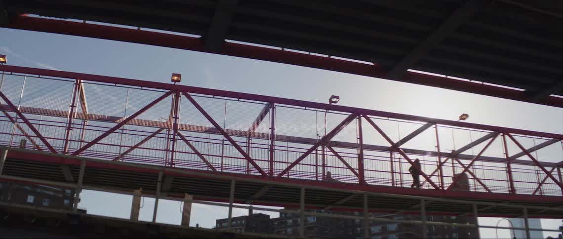 A person is jogging across a bridge as a train passes by below and there are buildings in the distance
