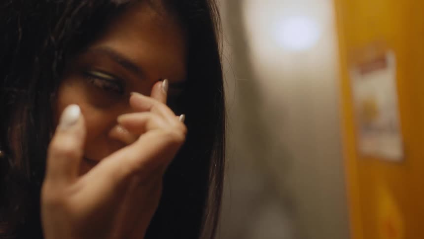 An indian woman uses her finger to dab a small amount of paint and apply it to her forehead