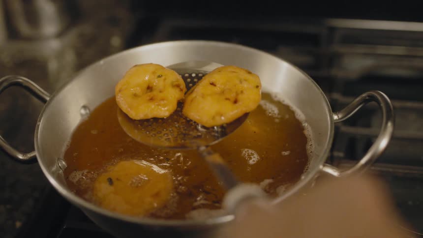 A hand holding a spatula removes fried dough from the oil and places on paper towels in a colander
