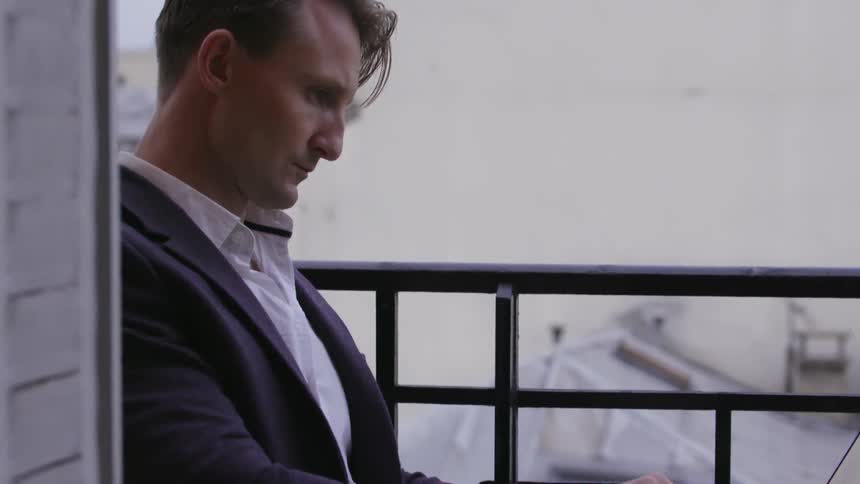Man typing on a laptop while sitting on an outdoor terrace