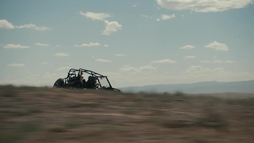 Four people with helmet drives off road vehicle across the plain