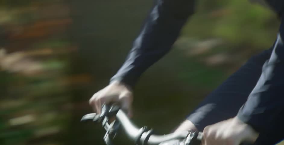 A male bicyclist pedals very quickly as he speeds along a path lined with trees