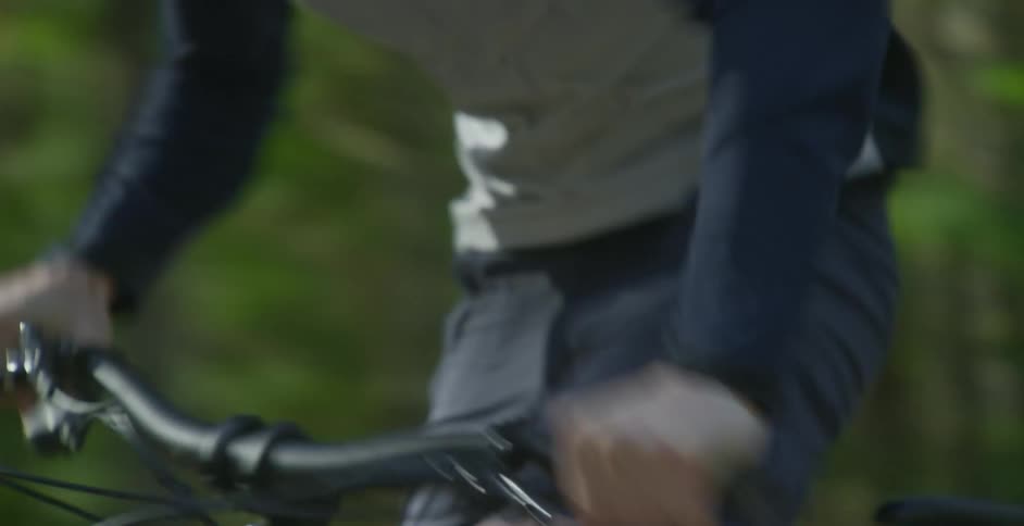 A male bicyclist pedals very quickly as he speeds along a path lined with trees and vegetation