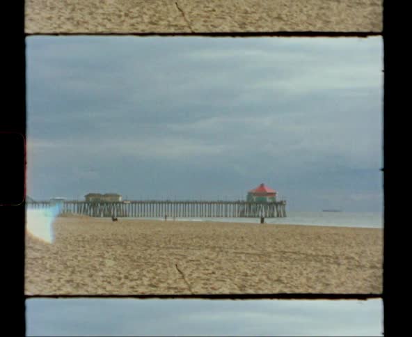 Person stands on beach as others move past pier
