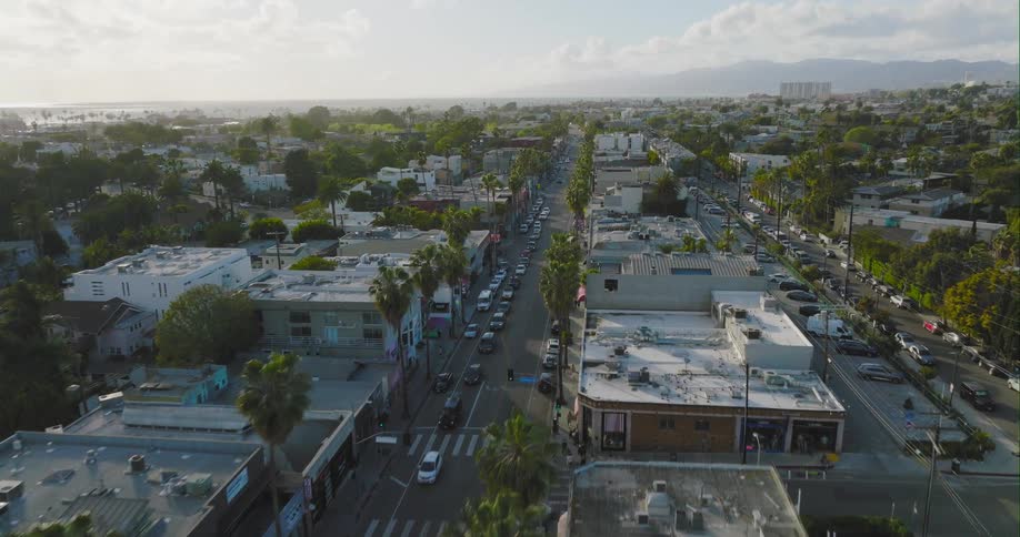 An aerial view of cars driving and parked along a street with stores and a few pedestrians walking along