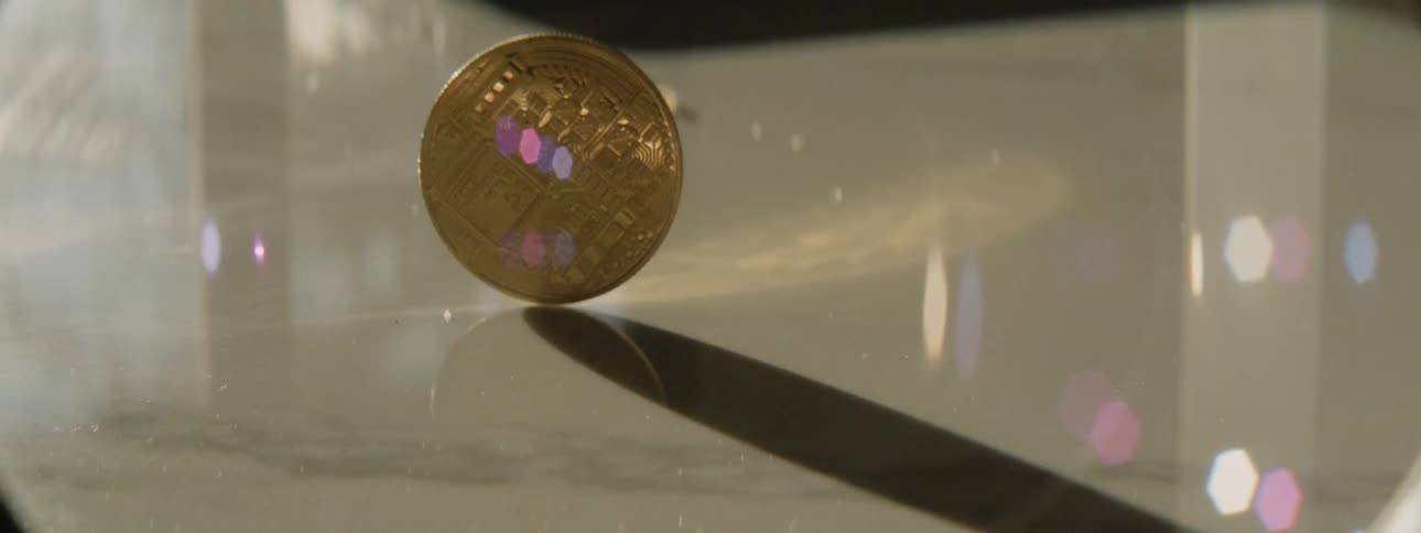 A person spins a large coin with the bitcoin symbol on the surface of a table