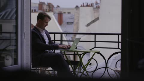 Man works on a laptop on a balcony
