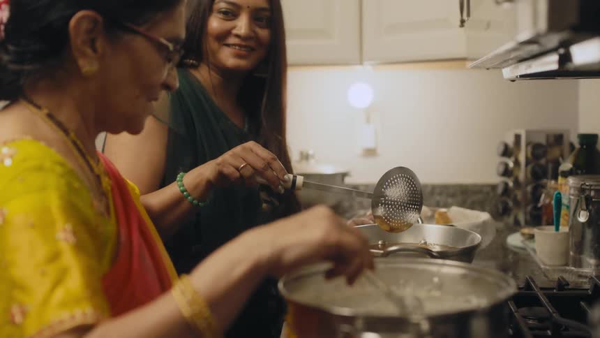 Woman and adult daughter stand in kitchen cooking while talking