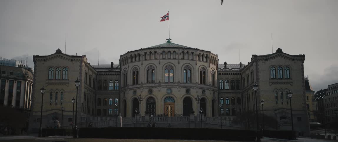 Front facade of the Storting Building of the Norwegian Parliament, called Stortingsbygningen, with the flag of Norway flying above.