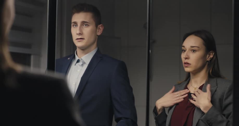 A man and woman are looking in a mirror and fixing their outfits and they kiss and walk away