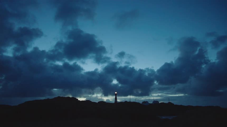 Distant view of lighthouse silhouetted against the cloudy sky at dusk
