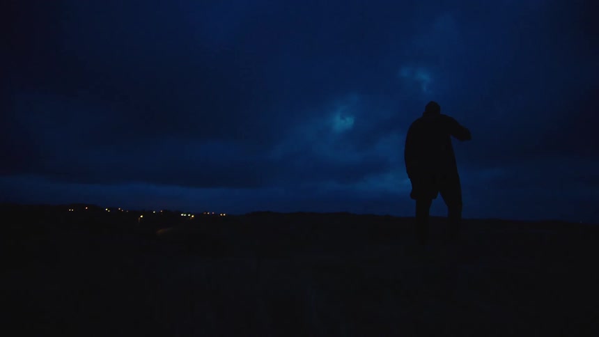 The silhouette of a man walking on a ridge stopping to look around in the wind