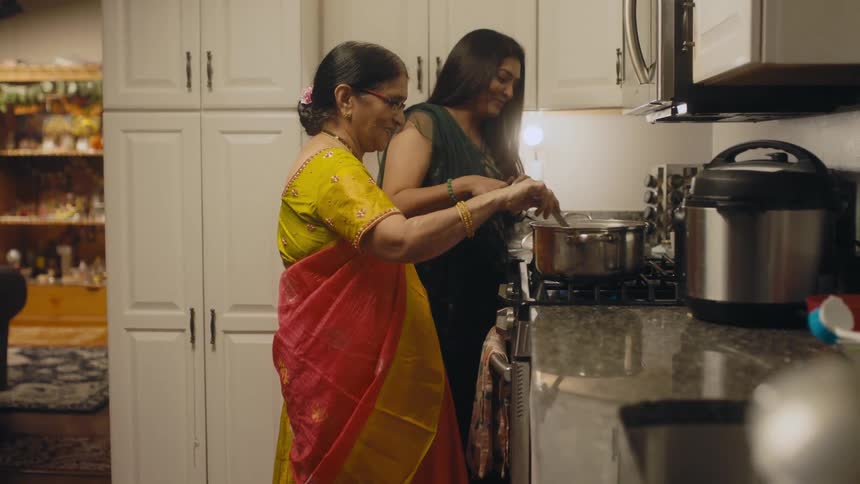 A mother and daughter smile as they cook together in a kitchen