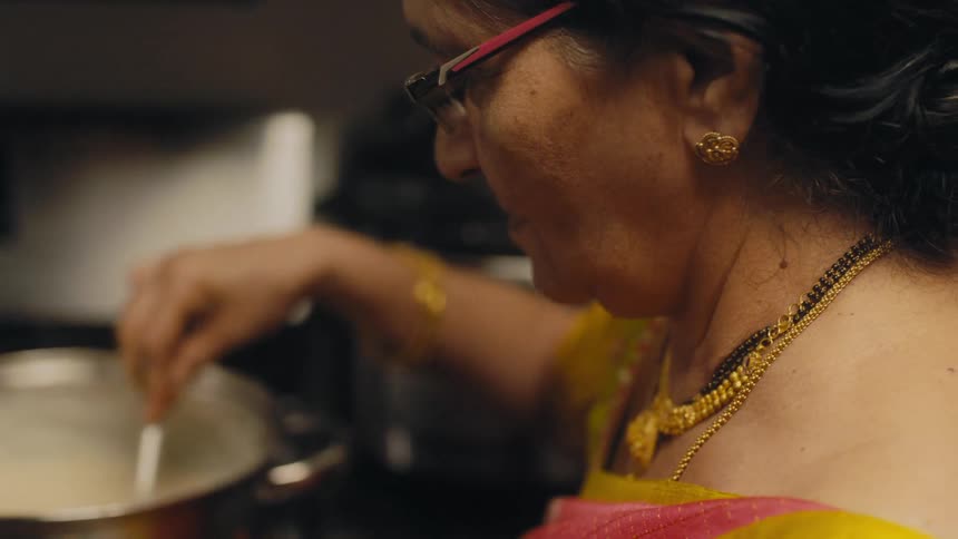 An indian woman wearing a sari stirs a pot on the stove