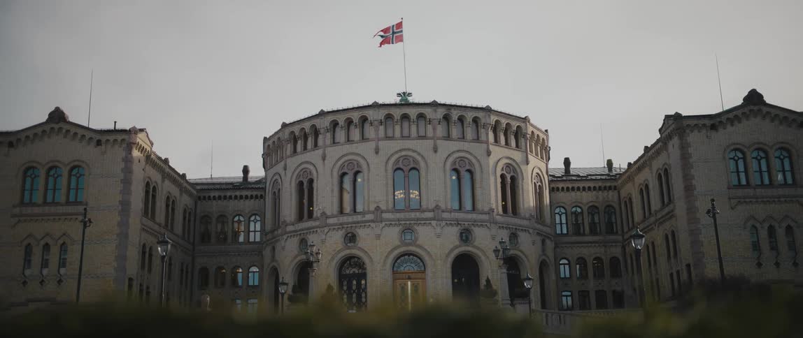 View from behind hedges of the Storting Building of the Norwegian Parliament, with the flag of Norway flying above.