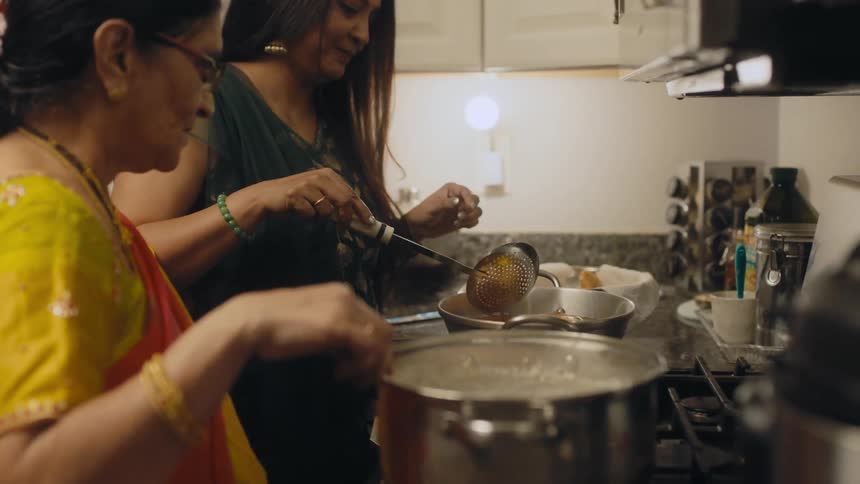 Two women are in a kitchen cooking and stirring the pots