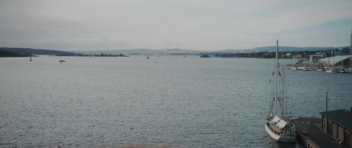 View looking out toward the quiet Oslo Fjord in Oslo, Norway on a cloudy day, with a small sailboat at dock in the corner.