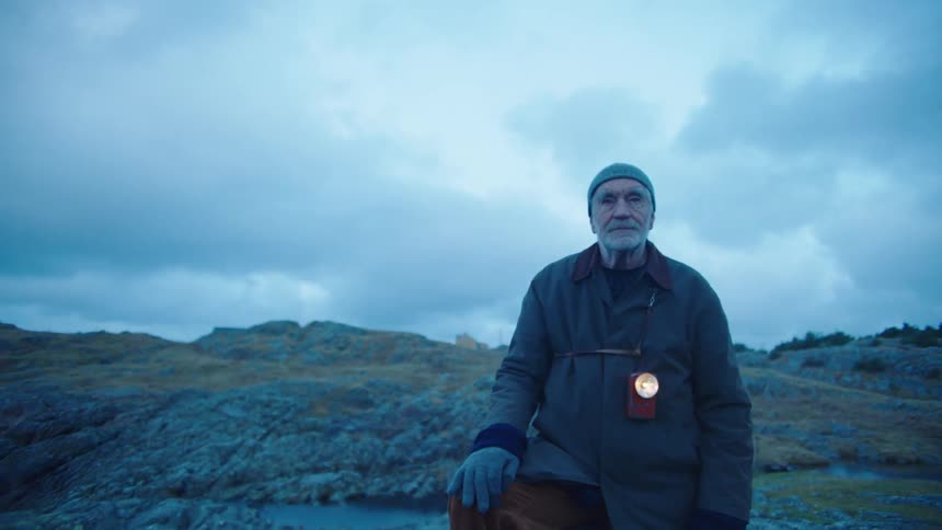An elderly man hiking over rocks in nature on a cloudy day