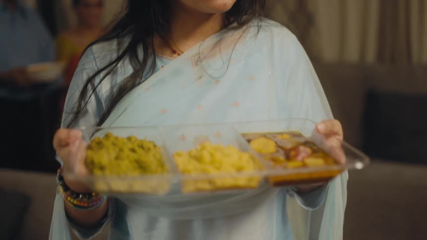 A woman with long dark hair and wearing a light blue gown is carrying a tray of food